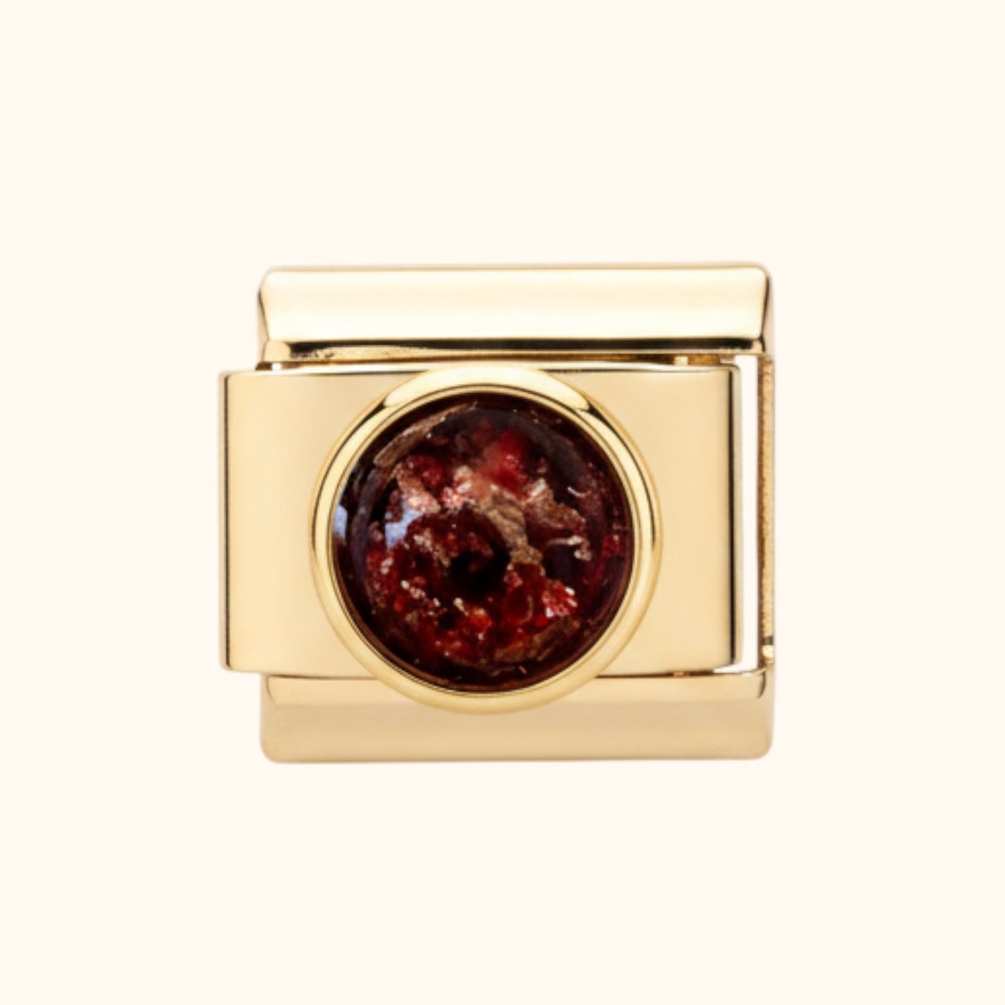 Gold charm with a red stone on a white background