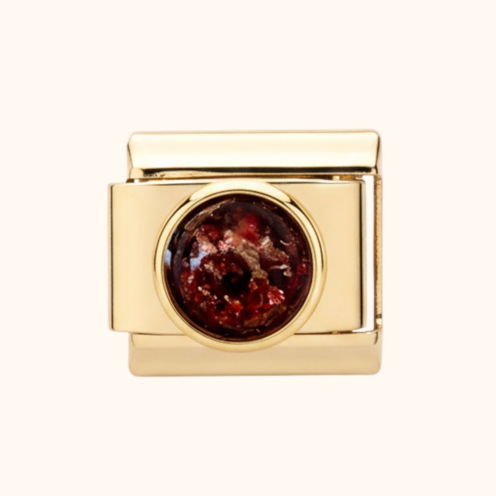 Gold charm with a red stone on a white background