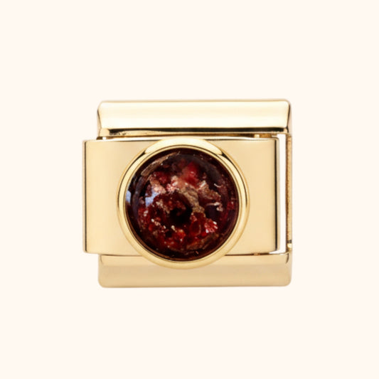 Gold charm with a red stone on a white background